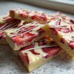 A stack of No-Bake Lemon Strawberry Cheesecake Bark squares topped with a white chocolate drizzle.