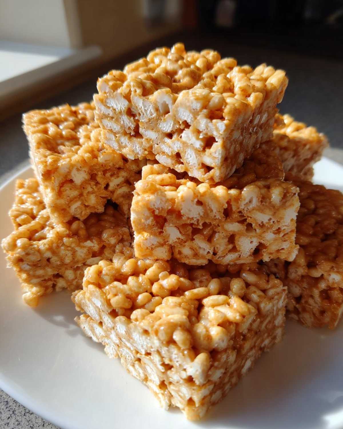 A close-up stack of golden, chewy No-Bake Peanut Butter Rice Cereal Bars on a white plate.