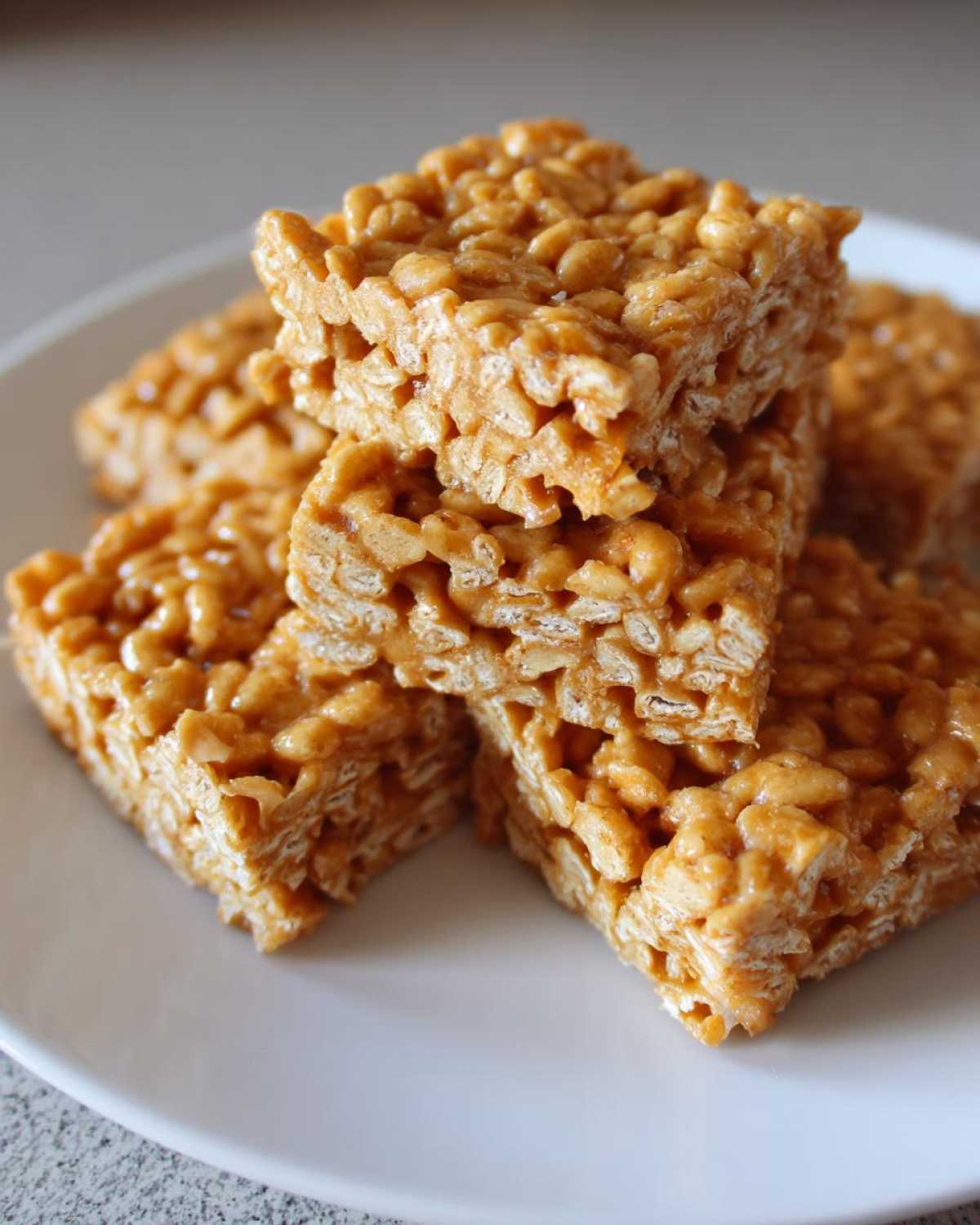 A close-up stack of chewy No-Bake Peanut Butter Rice Cereal Bars on a white plate.