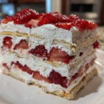 A tall, layered slice of No-Bake Strawberry Lemon Icebox Cake featuring whipped cream, graham crackers, and fresh strawberries.