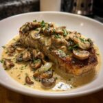 A perfectly seared pork chop smothered in creamy Dijon sauce, sautéed mushrooms, and onions, garnished with parsley.