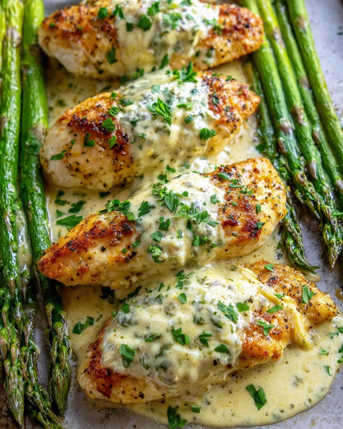 Four pieces of seared fish covered in creamy garlic butter sauce and parsley, served alongside roasted asparagus.