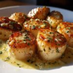 Close-up of seared scallops swimming in a creamy lemon butter sauce, garnished with parsley.