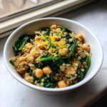 A white bowl filled with a vibrant One Pot Chickpea Quinoa Recipe, mixed with spinach and topped with lemon zest.