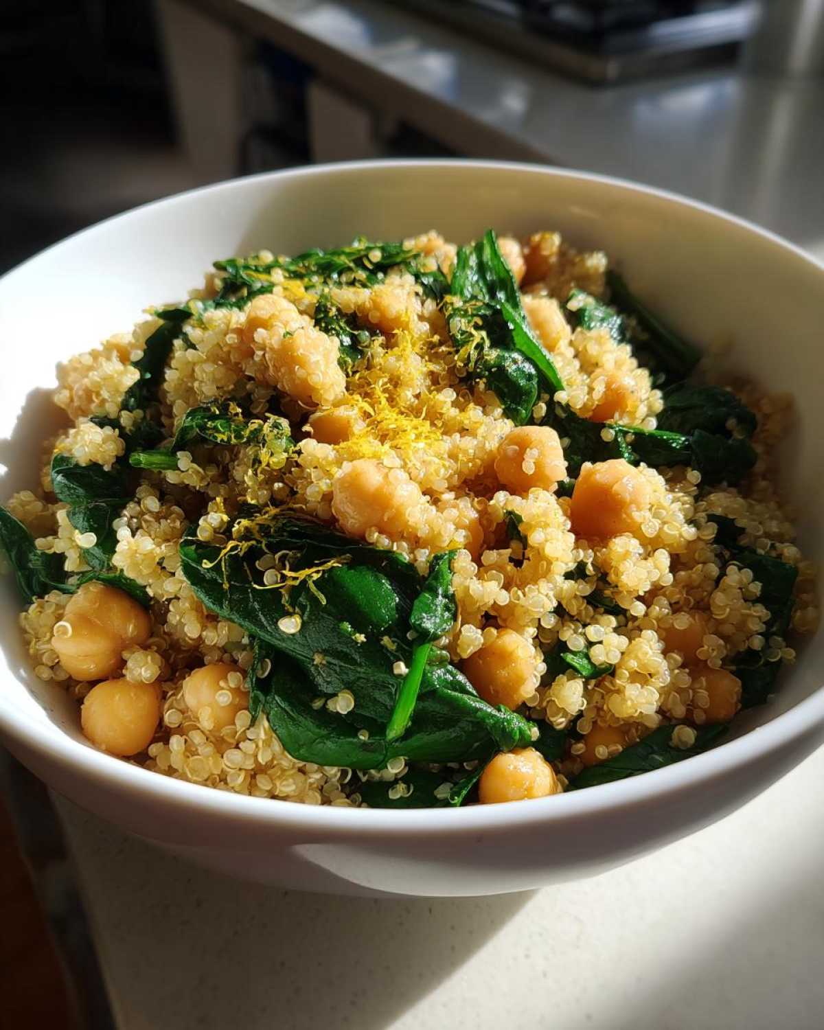 Close-up of a white bowl filled with the One Pot Chickpea Quinoa Recipe, mixed with spinach and topped with lemon zest.
