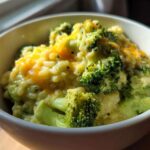 Close-up of a white bowl filled with One-Pot Creamy Broccoli Cheddar Rice topped with melted cheddar cheese.