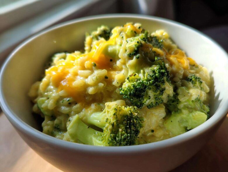 Close-up of a white bowl filled with One-Pot Creamy Broccoli Cheddar Rice topped with melted cheddar cheese.