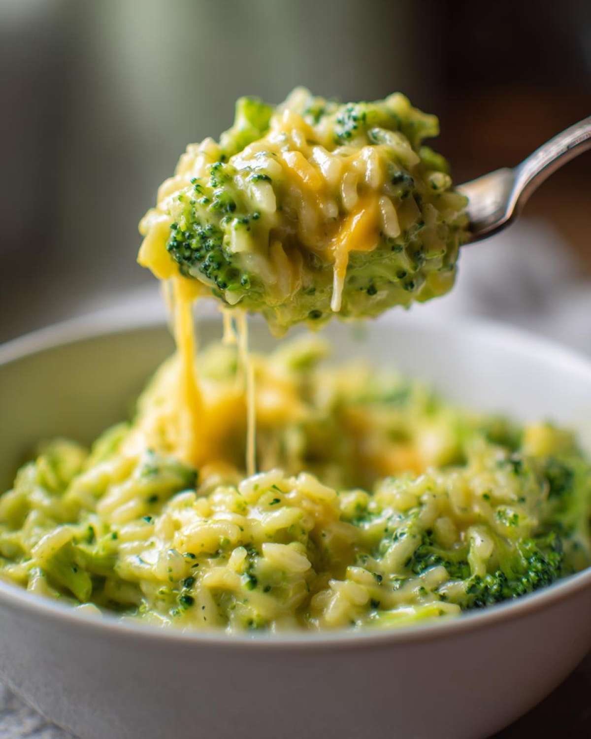 A fork lifts a cheesy, creamy spoonful of One-Pot Creamy Broccoli Cheddar Rice from a white bowl.