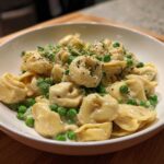 A close-up of One-Pot Creamy Garlic Butter Tortellini and Peas served in a white bowl, garnished with parsley.