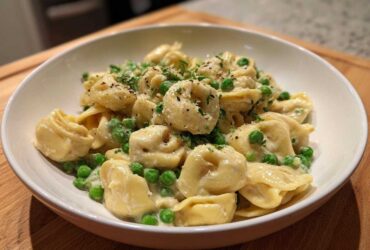A close-up of One-Pot Creamy Garlic Butter Tortellini and Peas served in a white bowl, garnished with parsley.