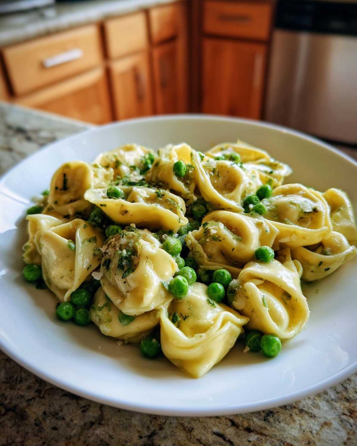 A close-up of a white bowl filled with One-Pot Creamy Garlic Butter Tortellini and Peas, garnished with herbs.