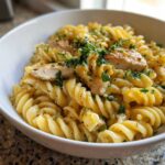 Close-up of a white bowl filled with One-Pot Creamy Lemon Pepper Chicken Pasta topped with sliced chicken and fresh parsley.
