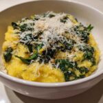 A close-up of One-Pot Creamy Spinach Parmesan Polenta topped generously with grated Parmesan cheese in a white bowl.