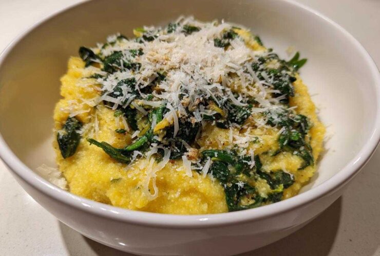 A close-up of One-Pot Creamy Spinach Parmesan Polenta topped generously with grated Parmesan cheese in a white bowl.
