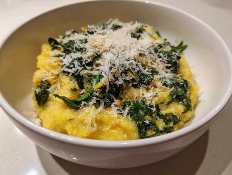 A close-up of One-Pot Creamy Spinach Parmesan Polenta topped generously with grated Parmesan cheese in a white bowl.