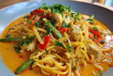A close-up of One-Pot Creamy Thai Red Curry Noodles featuring chicken, green beans, red peppers, and cilantro garnish in a rich orange sauce.