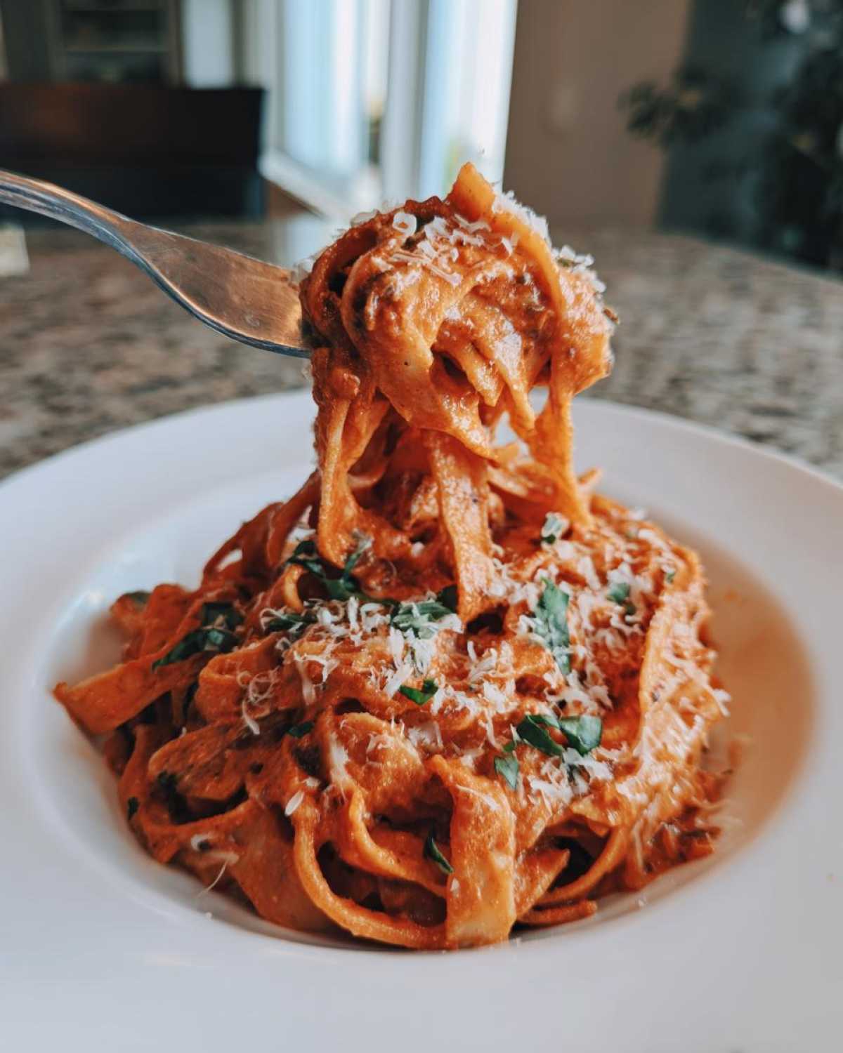 A fork lifting a generous portion of One-Pot Creamy Tomato Basil Tortilla Pasta, topped with Parmesan and basil.