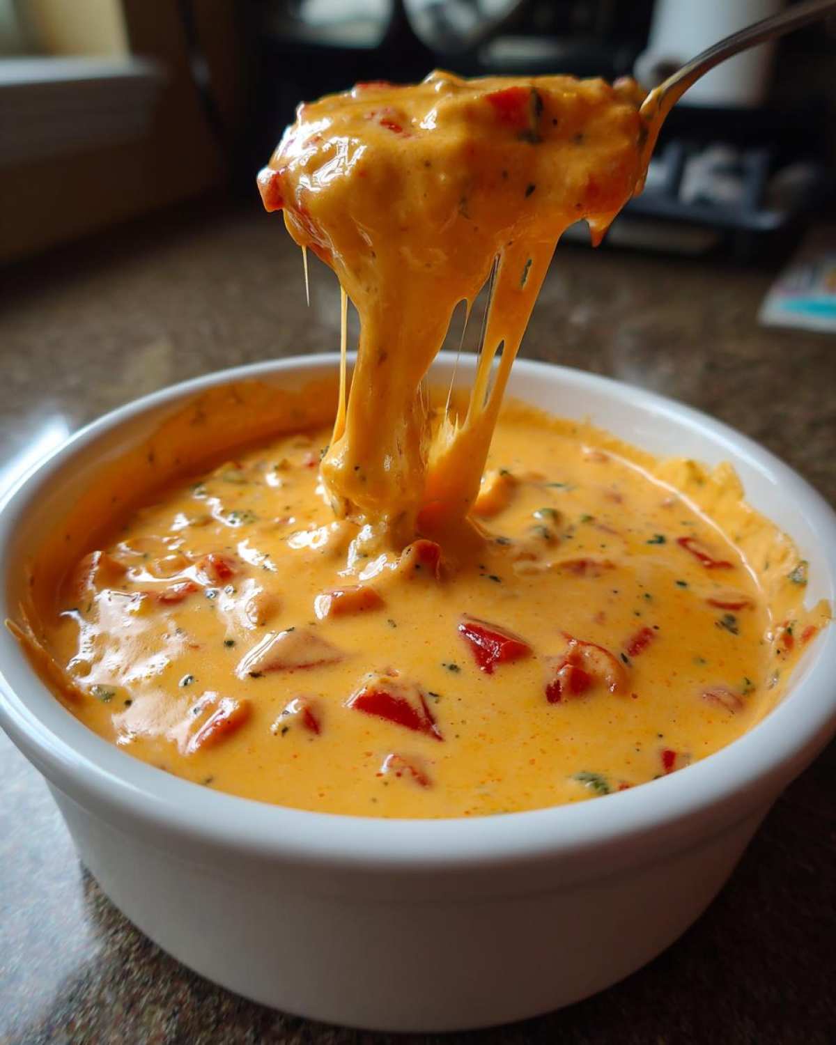A spoonful of rich, orange Queso Dip showing extreme cheese pull, served in a white bowl.
