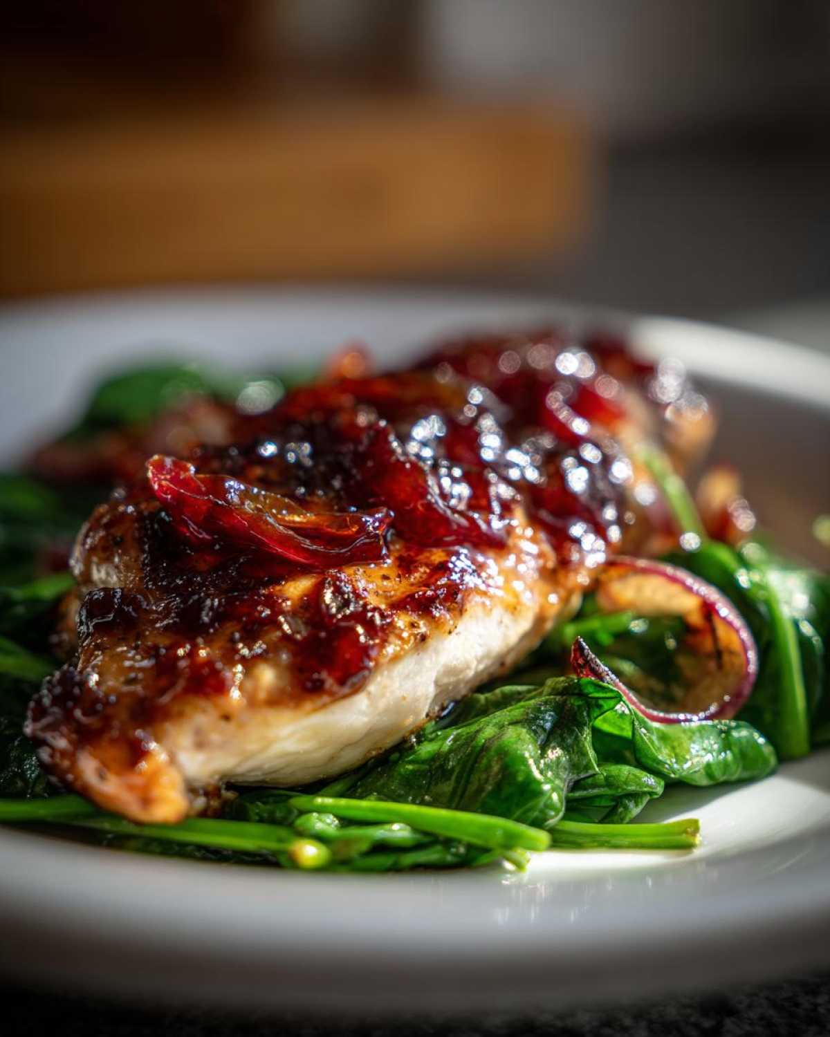 Close-up of Sheet Pan Balsamic Strawberry Chicken breast glazed with dark sauce, served over wilted spinach.