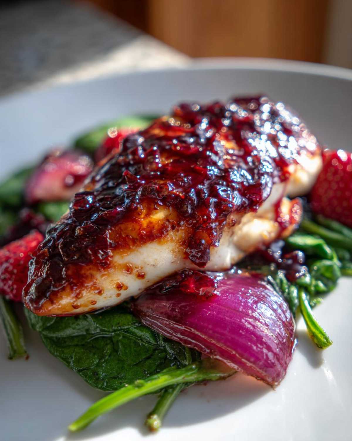 Close-up of Sheet Pan Balsamic Strawberry Chicken topped with a dark glaze, served over wilted spinach and red onion.