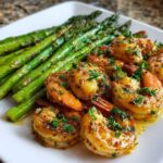 Close-up of juicy Sheet Pan Crispy Garlic Butter Shrimp and Asparagus glistening with butter sauce and topped with parsley.