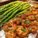 Close-up of Sheet Pan Crispy Garlic Butter Shrimp and Asparagus glistening with butter sauce and topped with parsley.