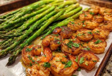 Close-up of Sheet Pan Crispy Garlic Butter Shrimp and Asparagus glistening with butter sauce and topped with parsley.