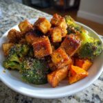 Close-up of crispy Sheet Pan Crispy Honey Mustard Tofu cubes served with roasted broccoli and sweet potatoes in a white bowl.