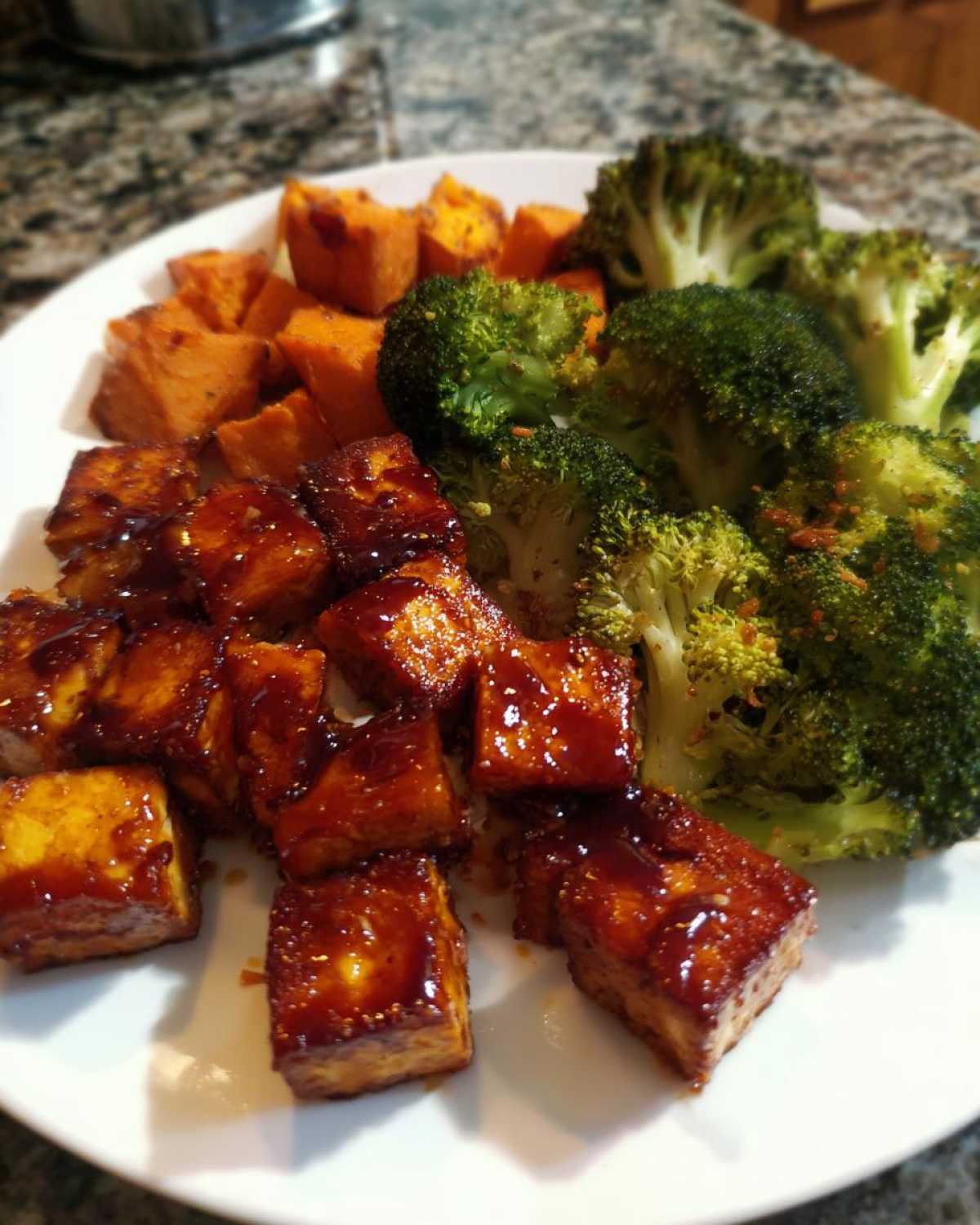 A white plate featuring crispy Sheet Pan Crispy Honey Mustard Tofu cubes alongside roasted sweet potatoes and bright green broccoli florets.