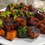 Close-up of glazed Sheet Pan Crispy Honey Mustard Tofu cubes served with roasted broccoli florets and sweet potato chunks.