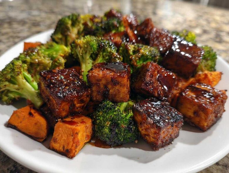 Close-up of glazed Sheet Pan Crispy Honey Mustard Tofu cubes served with roasted broccoli florets and sweet potato chunks.