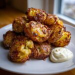A pile of golden brown, crispy smashed potatoes served on a white plate with a dollop of garlic aioli.