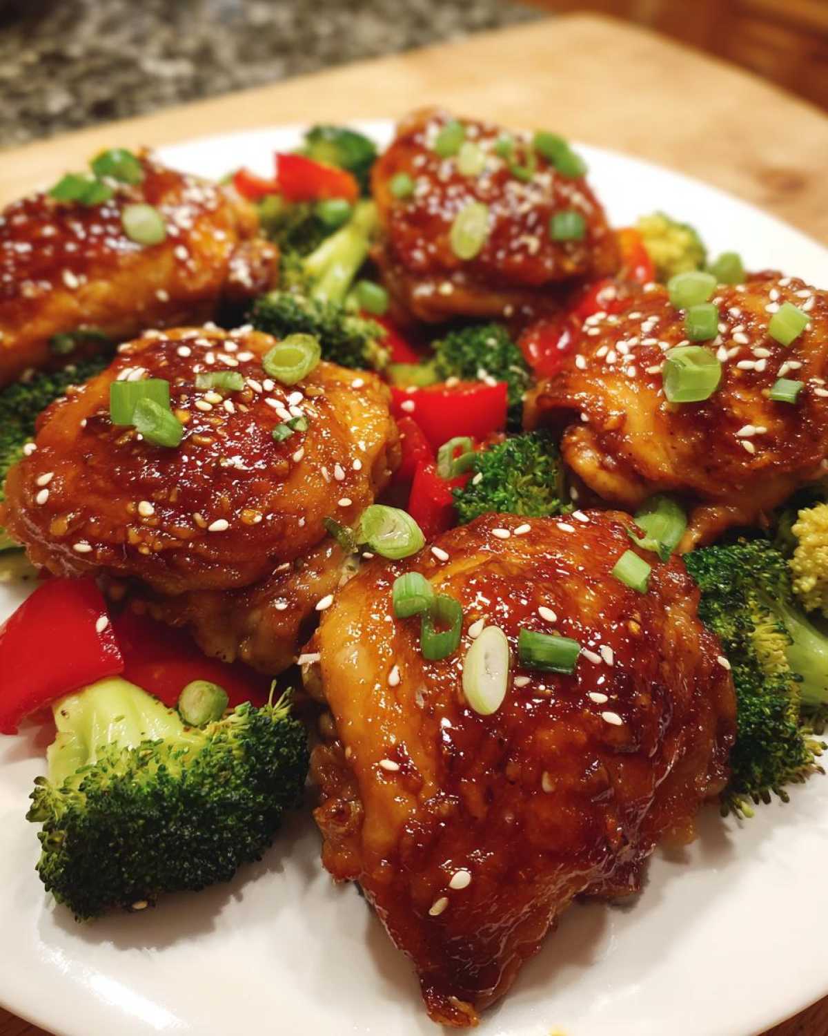 Close-up of glazed Sheet Pan Ginger Orange Chicken Thighs served over broccoli and red peppers, topped with sesame seeds.