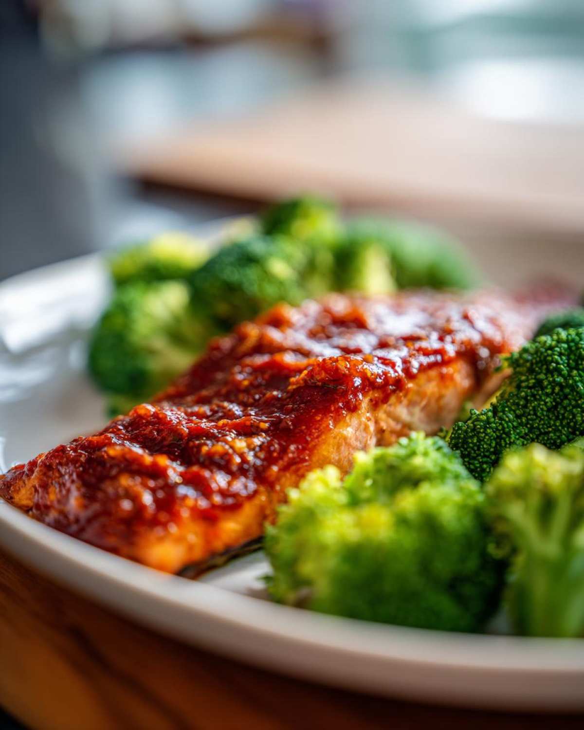 Close-up of a perfectly cooked fillet of Sheet Pan Honey Harissa Salmon topped with a rich red glaze, served alongside bright green broccoli florets.