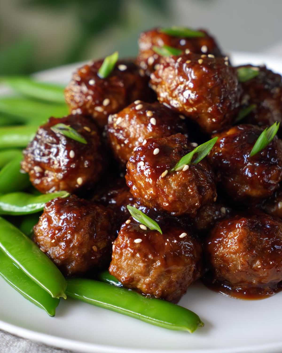 Close-up of Sheet Pan Sticky Sesame Meatballs coated in glaze and sprinkled with sesame seeds, served over bright green snap peas.