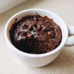 Close-up of a rich, dark chocolate Single Serve Protein Brownie topped with melted chocolate chips, baked in a white mug.