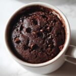 Overhead close-up of a rich, dark chocolate Single Serve Protein Brownie baked inside a white mug, topped with melted chocolate chips.