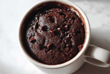 Overhead close-up of a rich, dark chocolate Single Serve Protein Brownie baked inside a white mug, topped with melted chocolate chips.