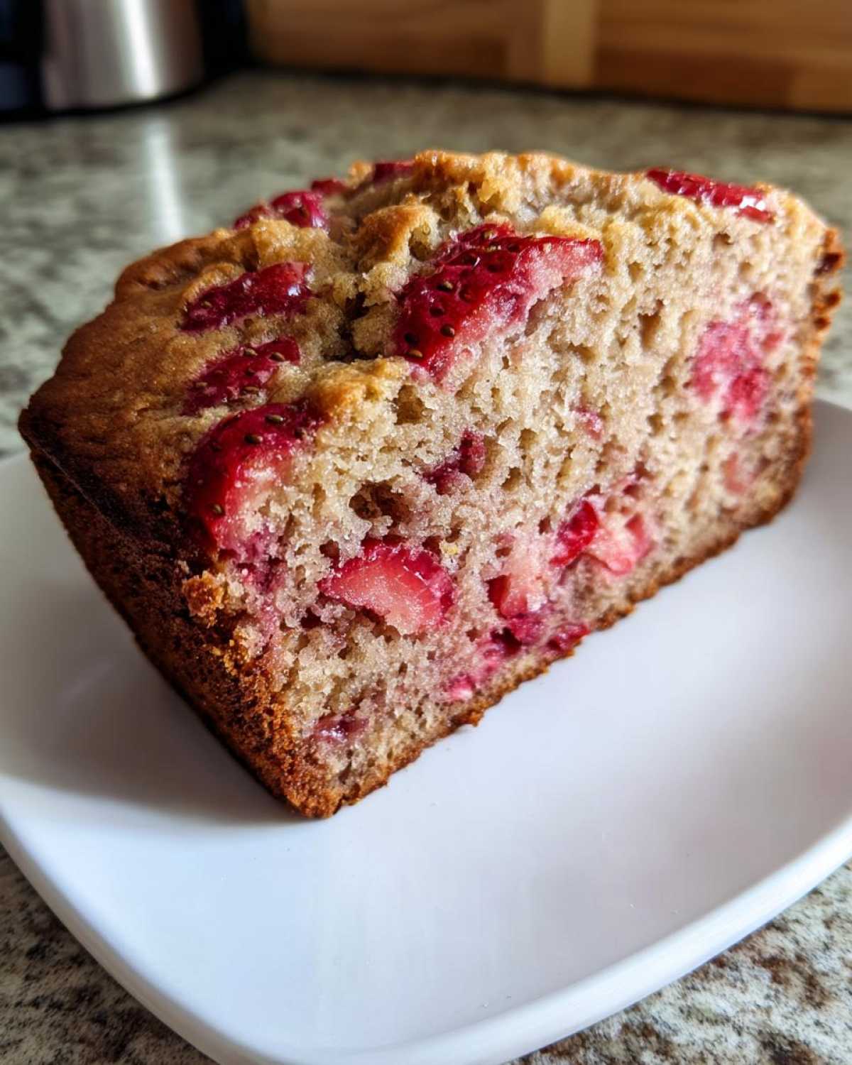 A close-up of a thick slice of moist Gluten-Free Strawberry Banana Bread showing baked strawberries throughout.