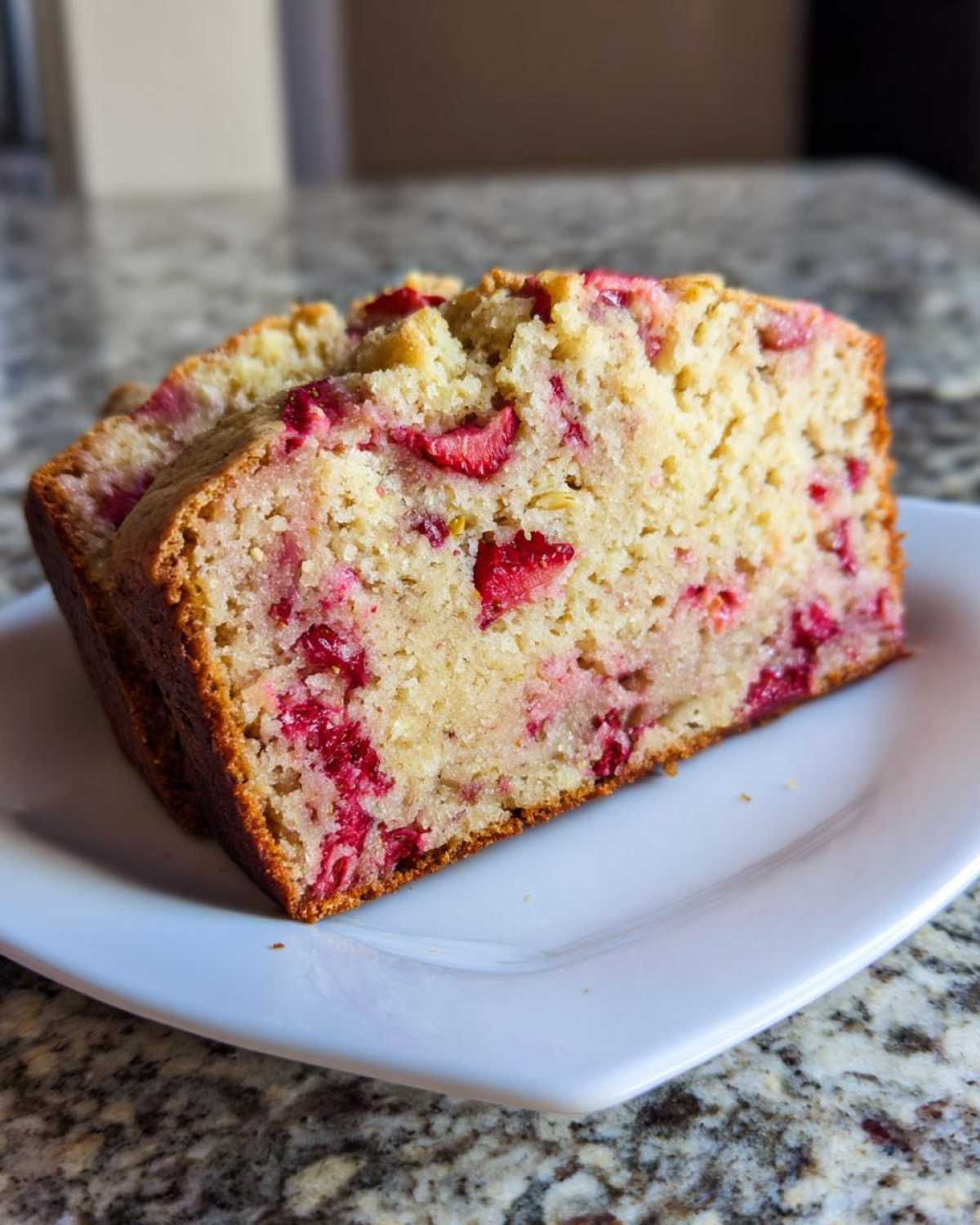 Close-up of a thick slice of Gluten-Free Strawberry Banana Bread showing bright red strawberry pieces baked throughout the moist crumb.