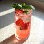 A tall glass filled with Sparkling Strawberry Basil Lemonade, featuring strawberry slices and basil garnish.