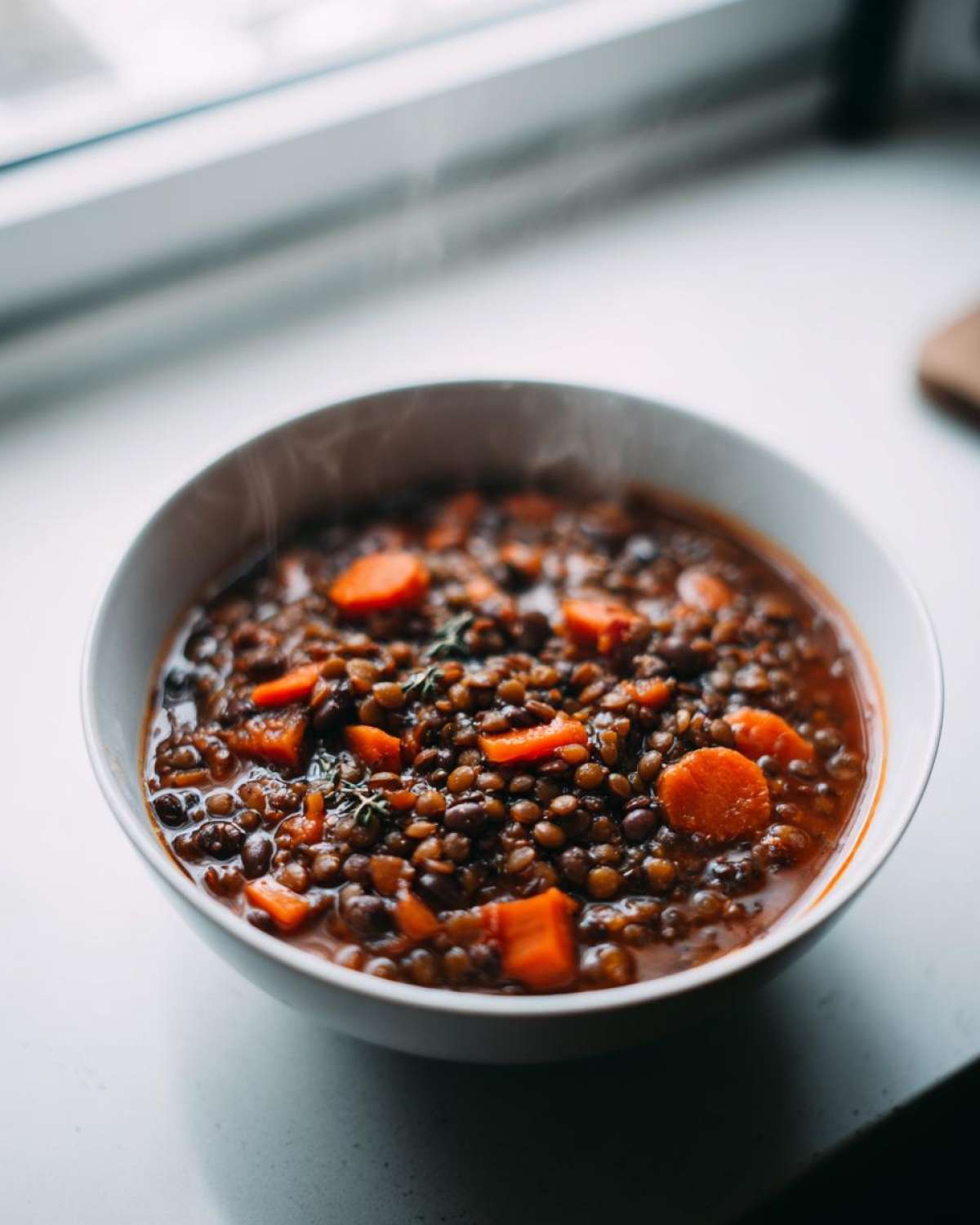 Close-up of a steaming white bowl filled with hearty Vegan One-Pot Lentil Taco Soup featuring dark lentils and bright orange carrot slices.