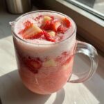 Close-up of a frosty glass mug filled with blended Strawberry Piña Colada Punch, topped with fresh strawberry slices and pineapple chunks.