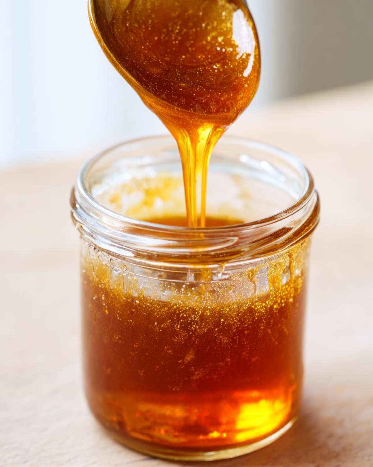 Close-up of thick, amber syrup being poured from a spoon into a small glass jar for Copycat Apple Cider Vinaigrette.