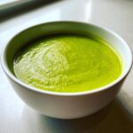 Close-up of a white bowl filled with bright green Vegan Creamy Cucumber Dill Soup.