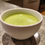 Close-up of a white bowl filled with bright green Vegan Creamy Cucumber Dill Soup, garnished with dill specks.
