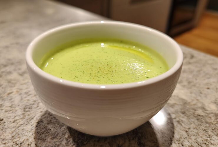 Close-up of a white bowl filled with bright green Vegan Creamy Cucumber Dill Soup, garnished with dill specks.