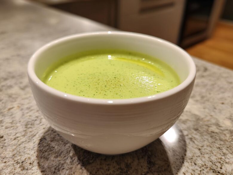 Close-up of a white bowl filled with bright green Vegan Creamy Cucumber Dill Soup, garnished with dill specks.