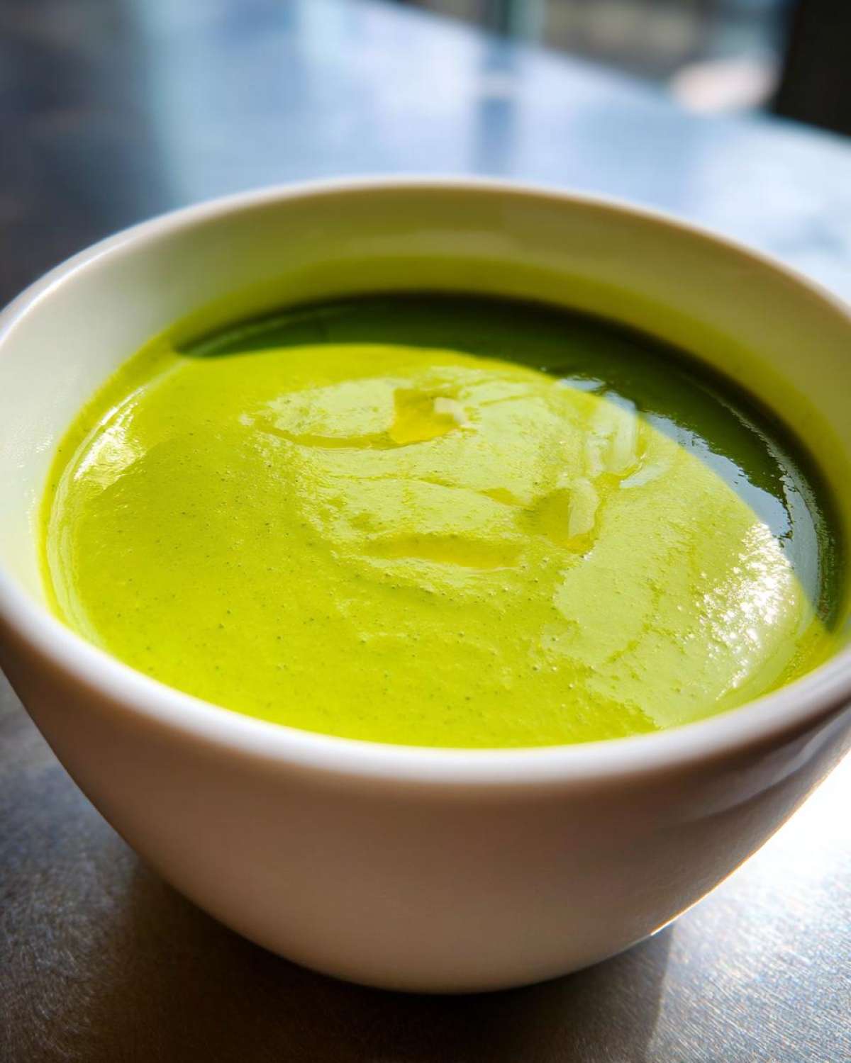 Close-up of vibrant green Vegan Creamy Cucumber Dill Soup in a white bowl, topped with a drizzle of oil.