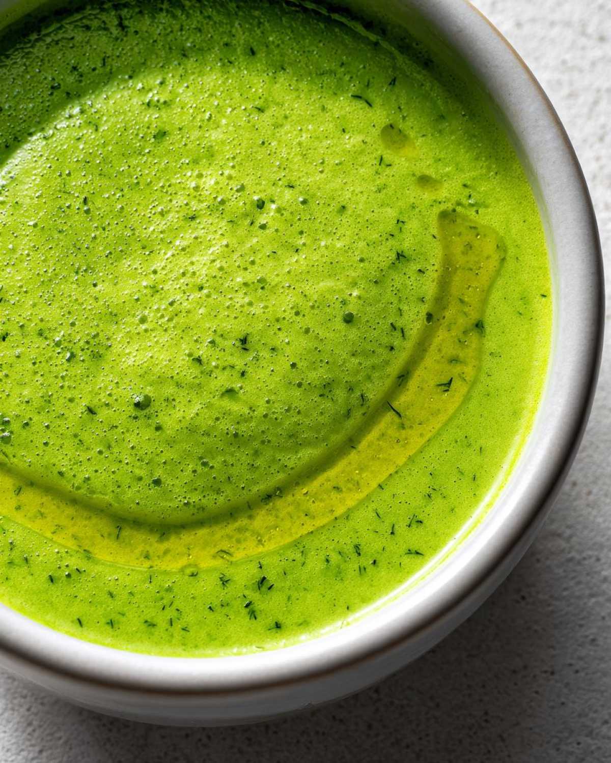 Close-up of bright green Vegan Creamy Cucumber Dill Soup topped with a swirl of olive oil and flecks of dill.